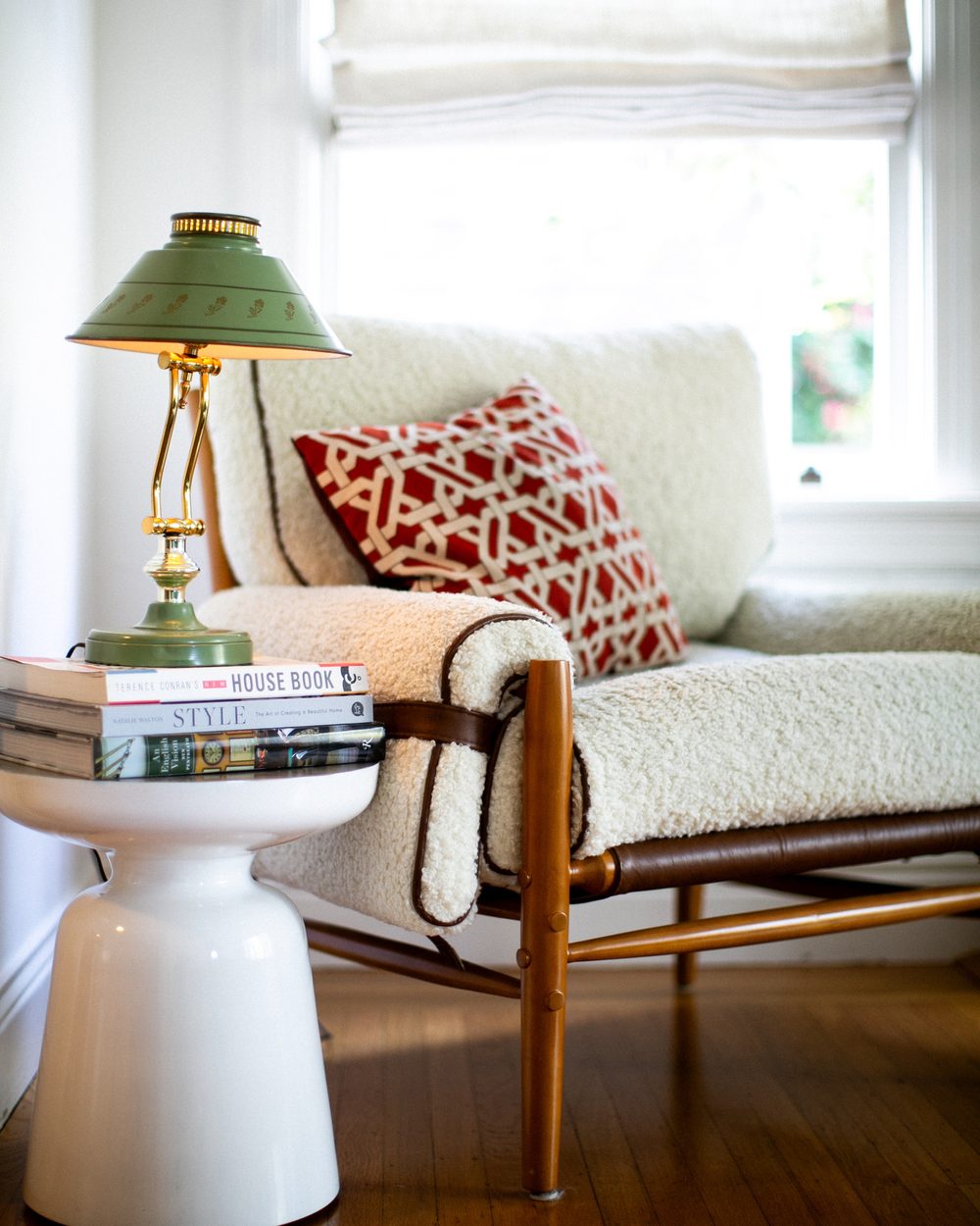 Cream boucle armchair with a red patterned pillow beside a green lamp
