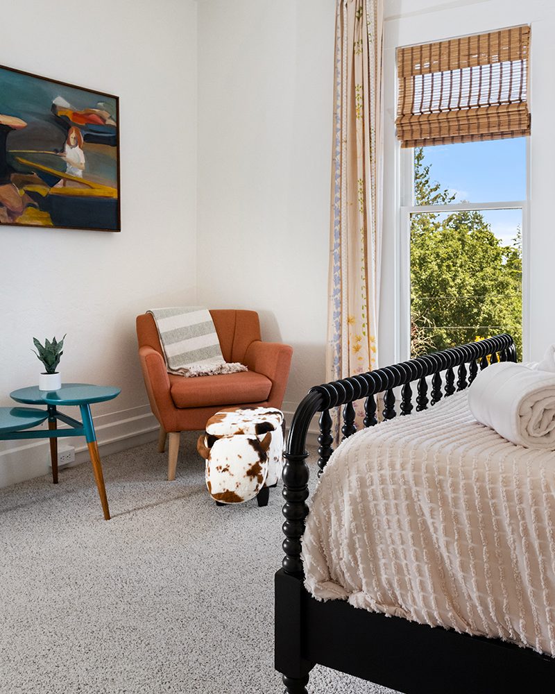 Bedroom with a spindle bed, orange armchair and painting