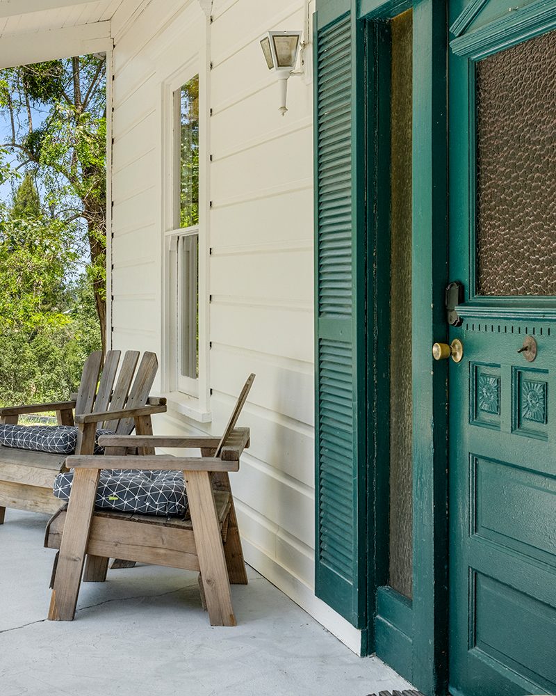 Front porch with wooden chairs and a green door